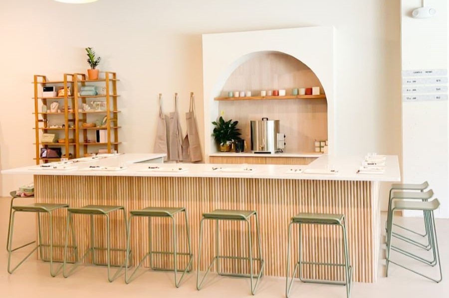 This bright, modern space features a sleek candle bar with inviting seating, minimalist decor, and a warm, creative ambiance perfect for hands-on crafting.